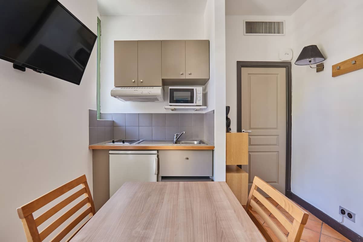 Una cocina compacta con microondas, lavamanos y un televisor montado en la pared.