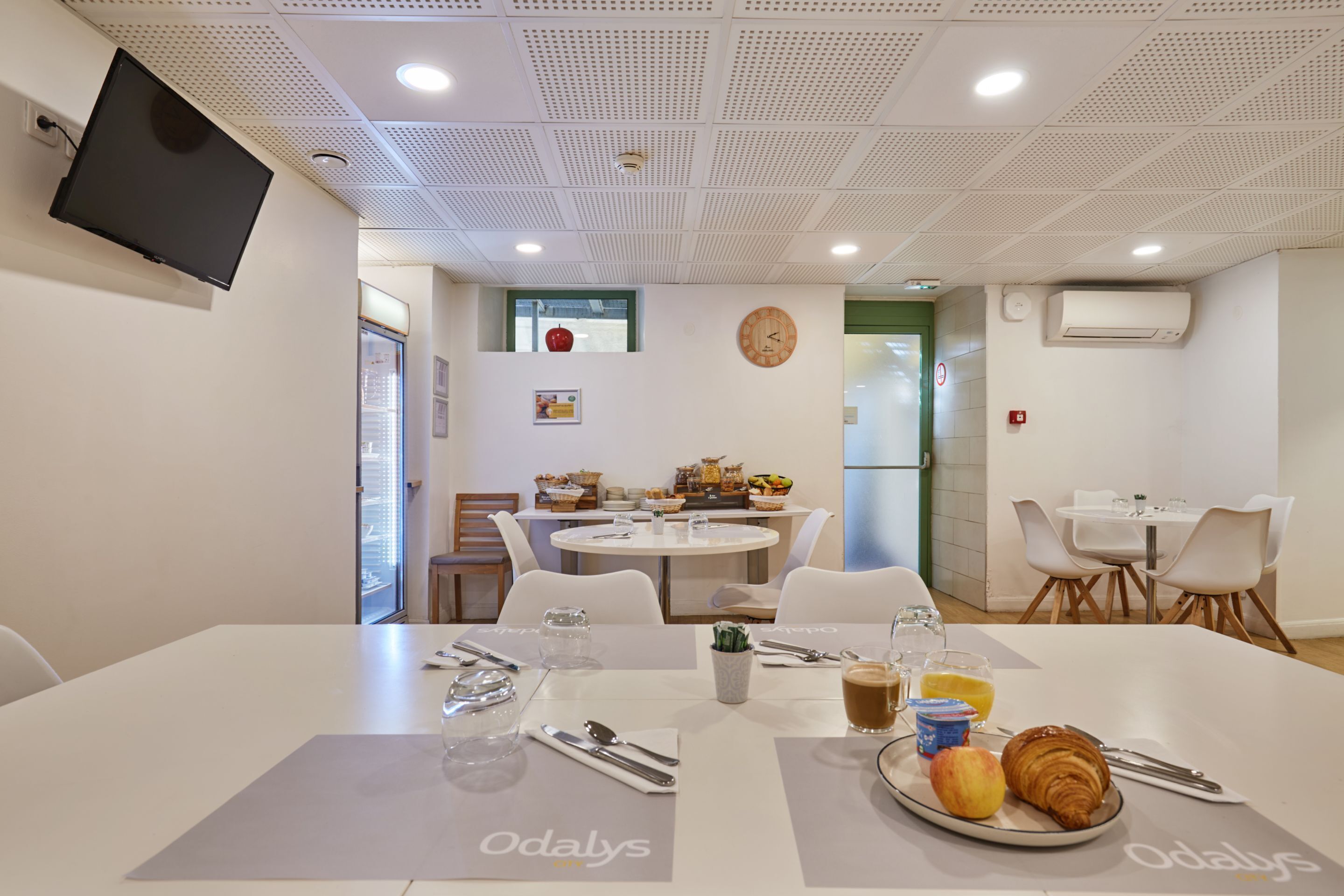 A dining area with tables set for breakfast, a clock on the wall, and an air conditioning unit.