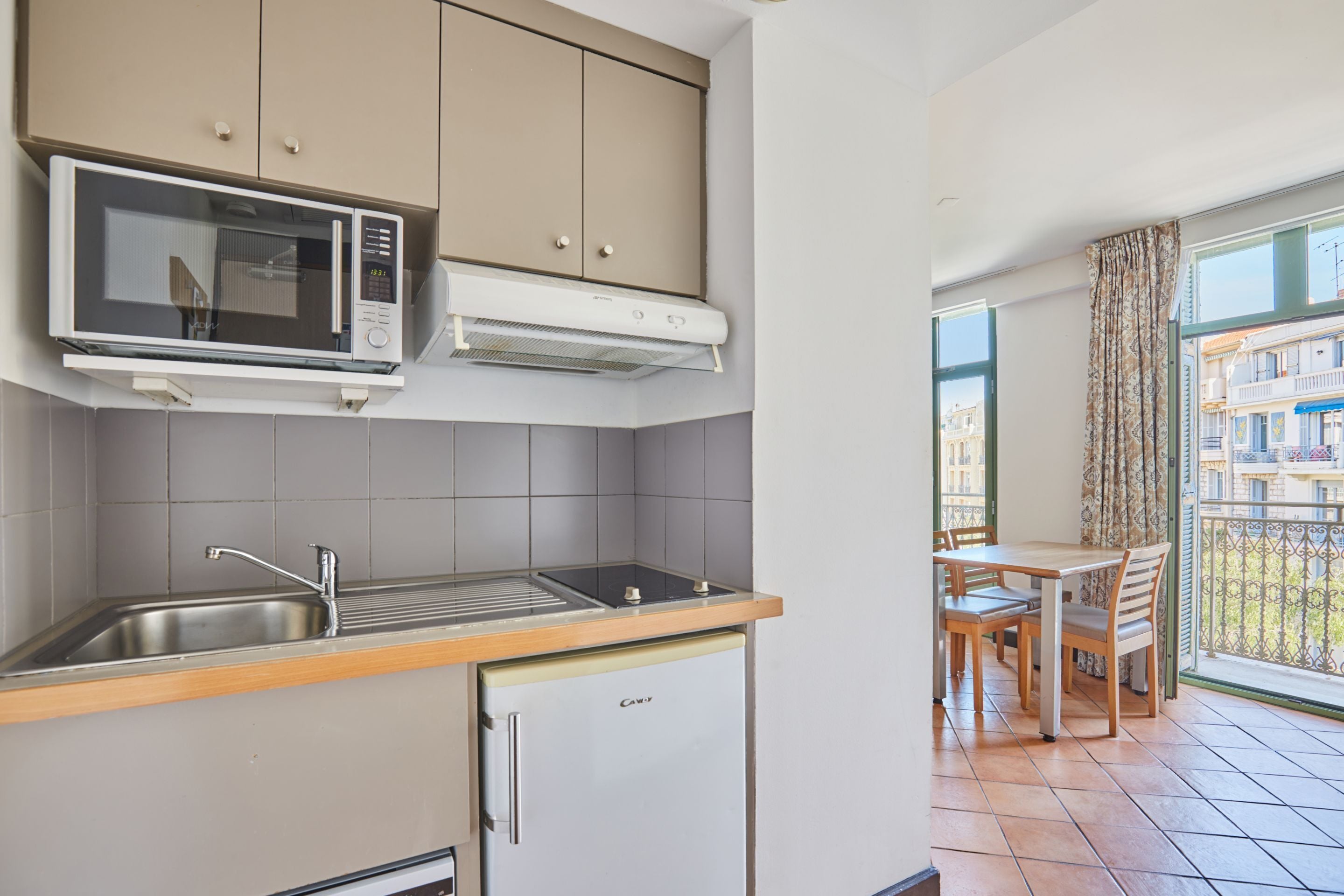 A compact kitchen with a microwave, sink, and small refrigerator. There is a dining area with a table and chairs.