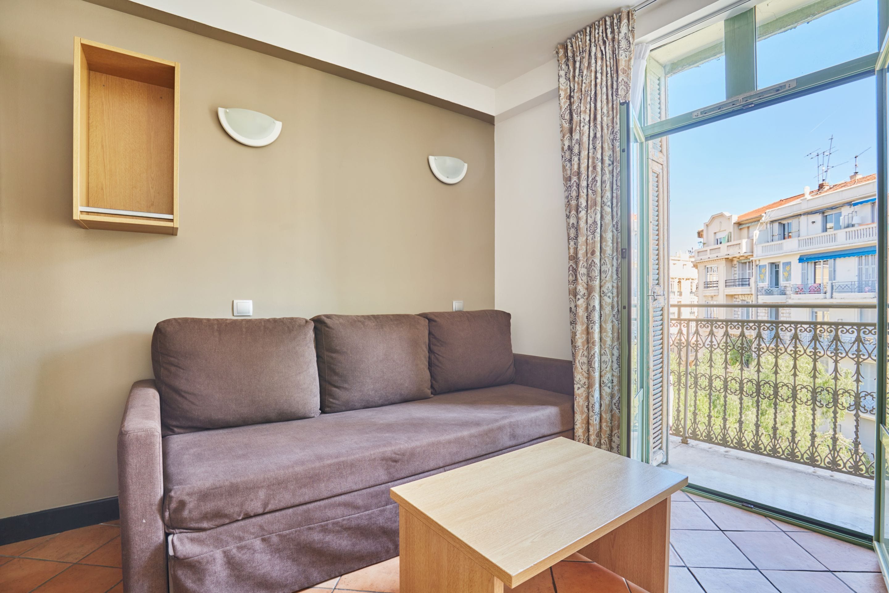 Een woonkamer met een bank, een houten tafel en een uitzicht op gebouwen door een raam.