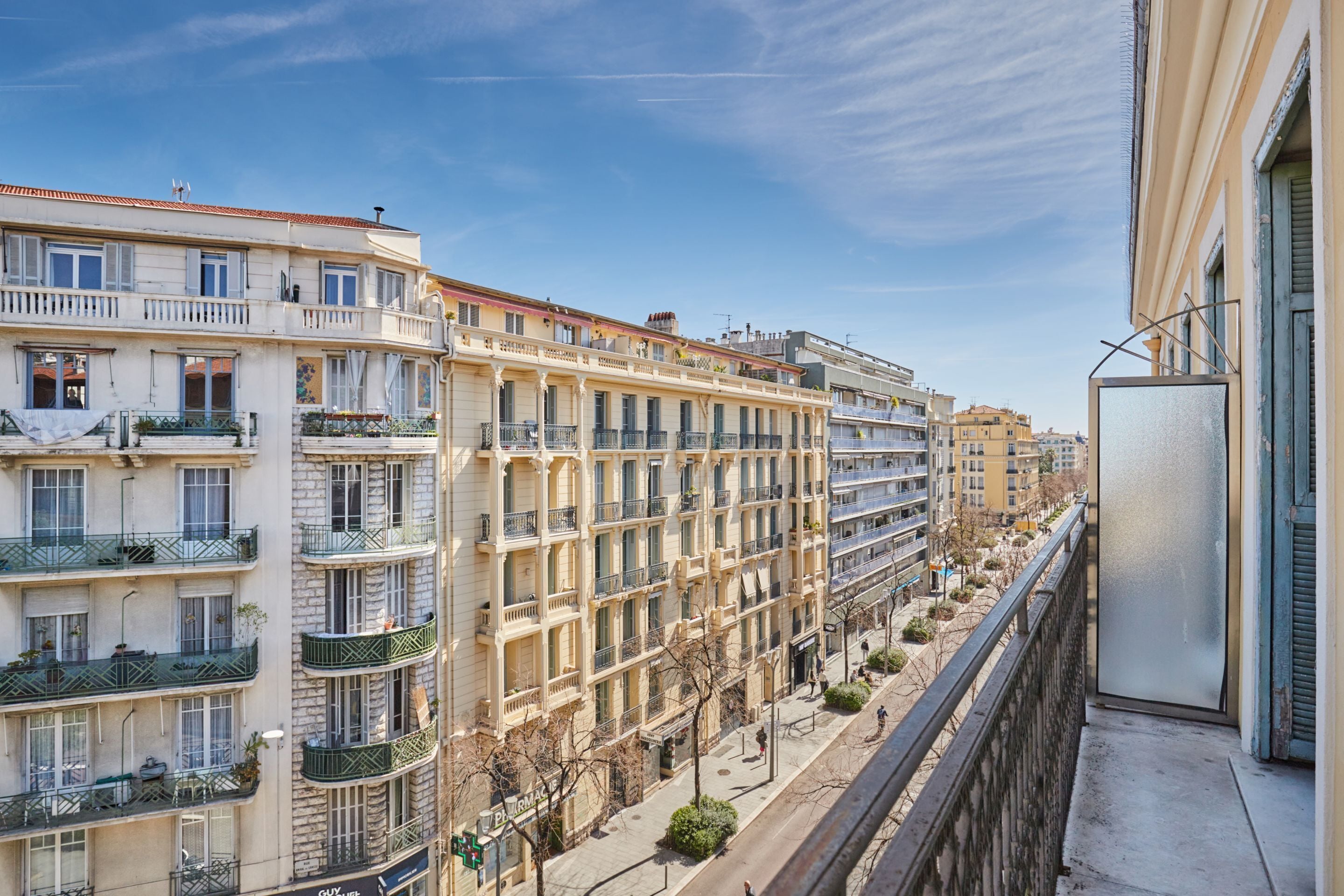 A multi-story building with balconies, a clear sky, and a street view.