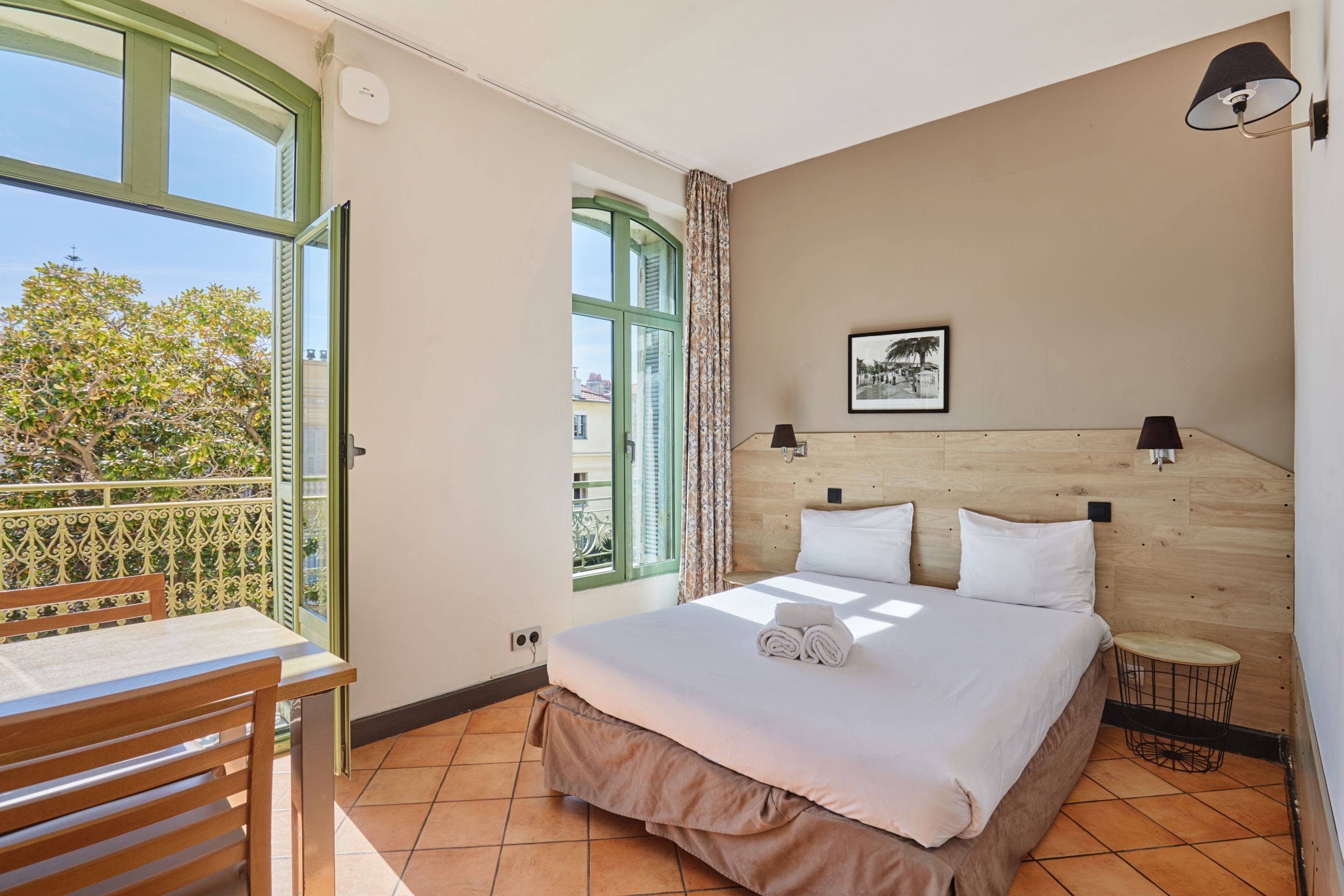 Een slaapkamer met een bed, een stoel, een klein tafeltje, een raam en een foto aan de muur.