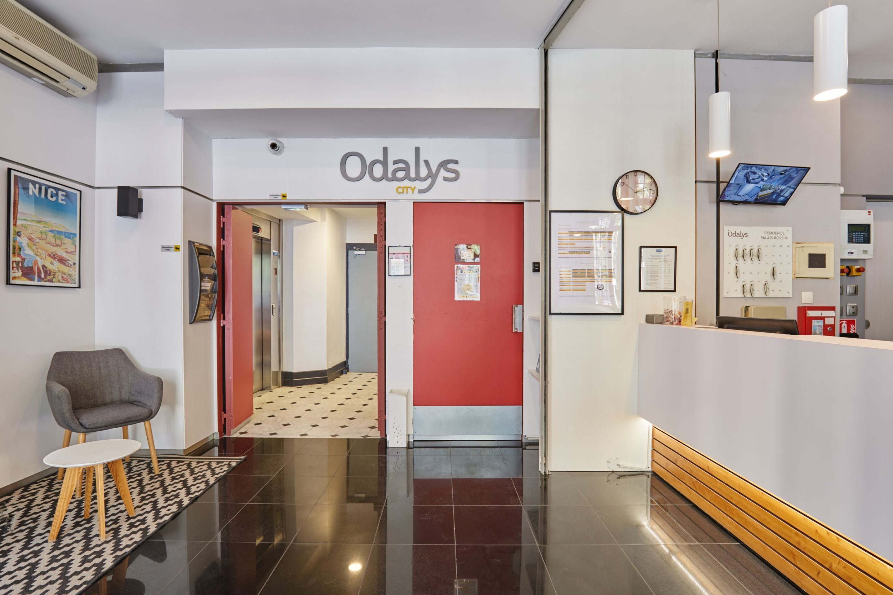 A reception area with a red wall, a reception desk, a clock, and a television screen.