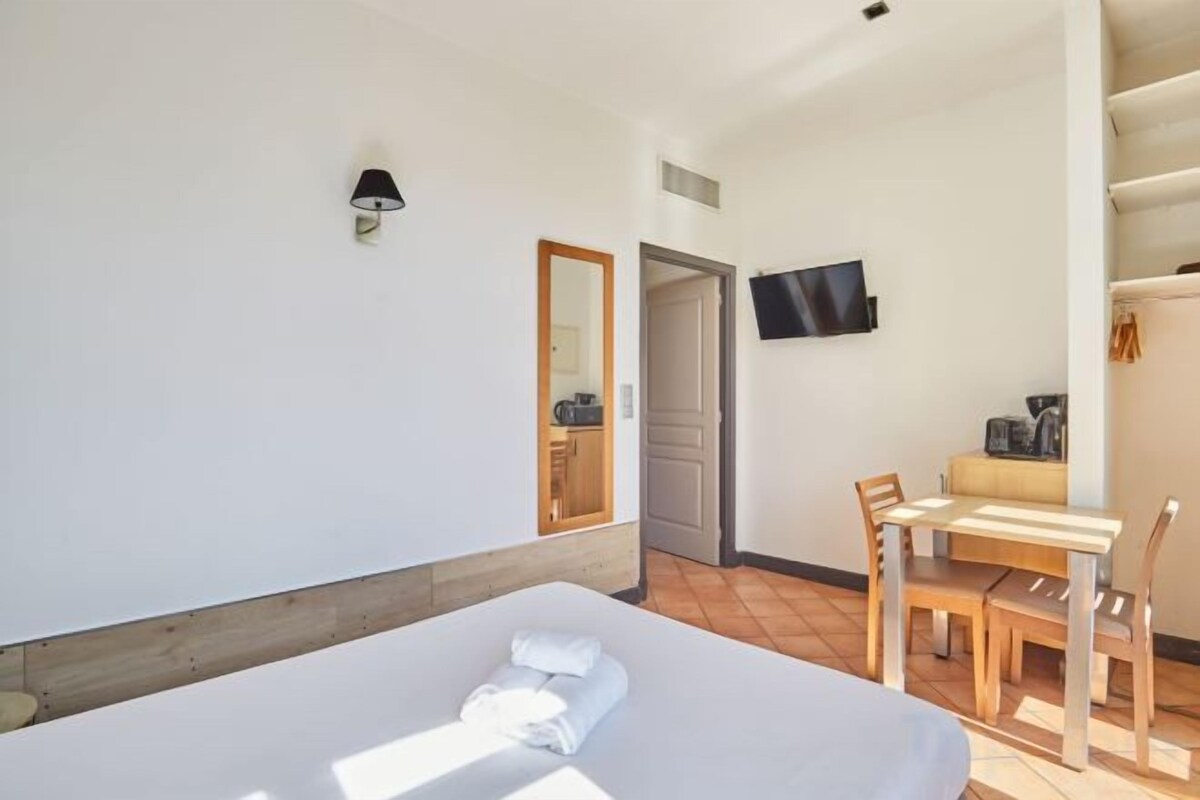 A hotel room with a bed, a desk, and a chair. There is a television mounted on the wall and a door leading to a bathroom.