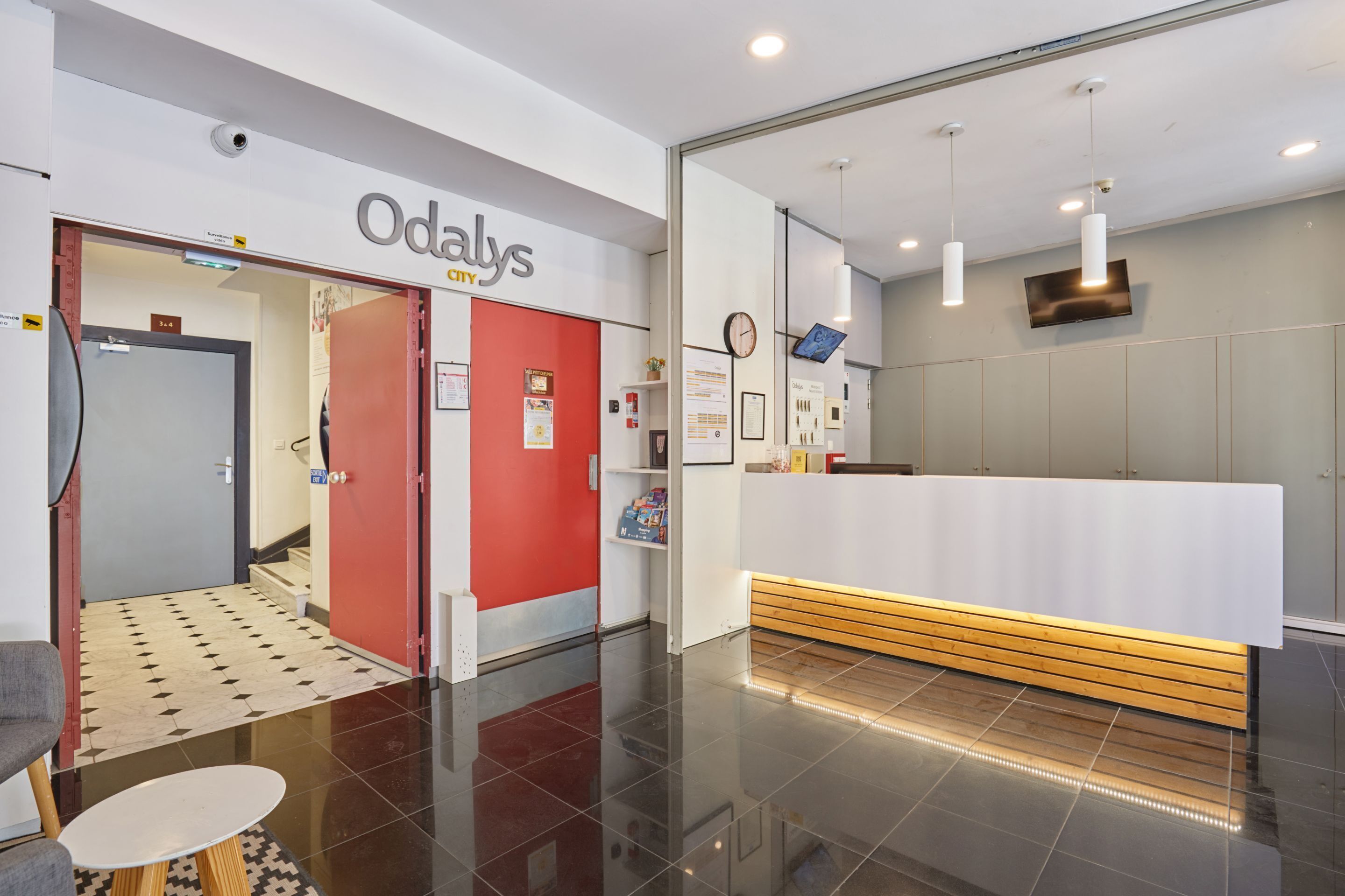 A reception area with a white reception desk, a red door, and a clock on the wall.