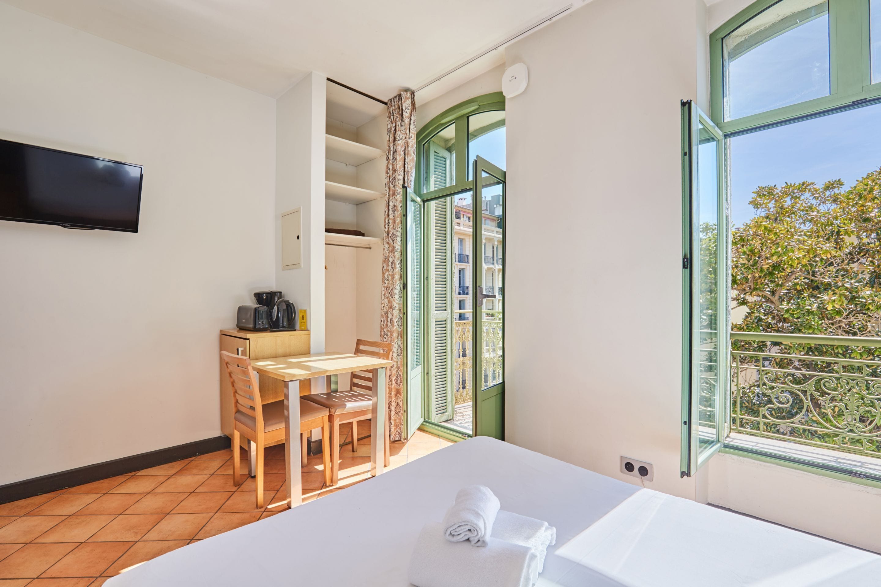 A hotel room with a bed, a desk with a chair, a television, and a balcony with a view.