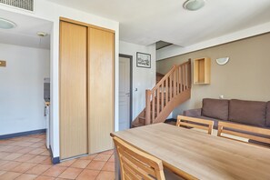 Un comedor con una mesa y sillas de madera, un sofá marrón, una escalera de madera y una puerta con panel de madera.
