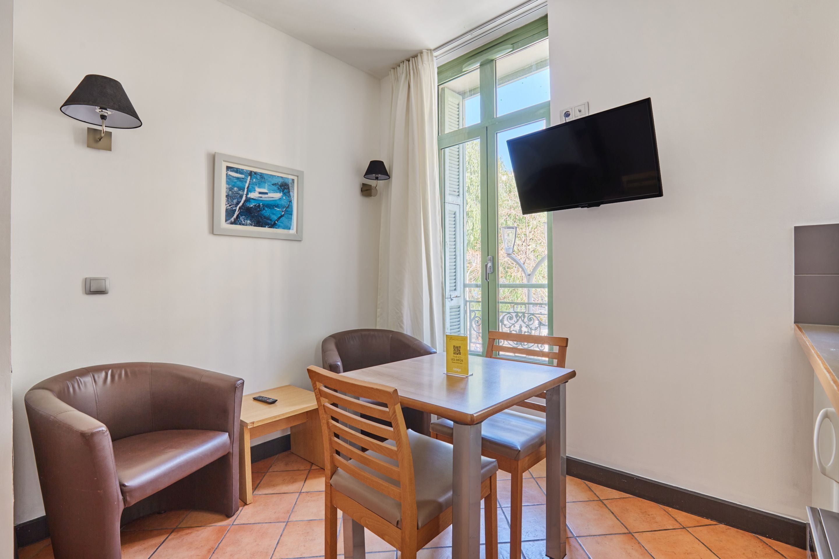 Una habitación con una mesa de madera, dos sillas, un sofá, un televisor, un cuadro y una ventana con cortinas.