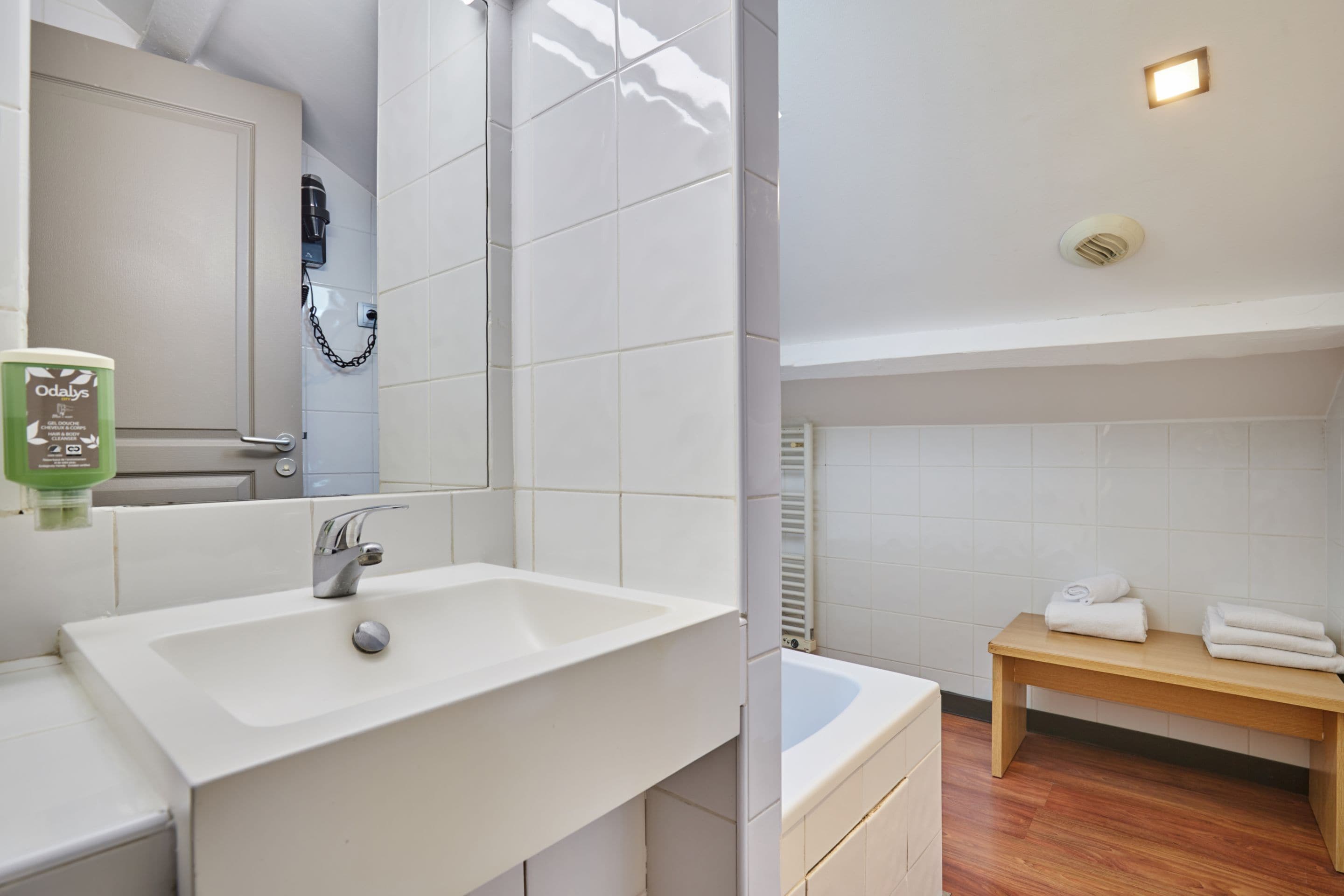 Une salle de bain avec un lavabo blanc, un miroir, un banc avec des serviettes et un espace douche.