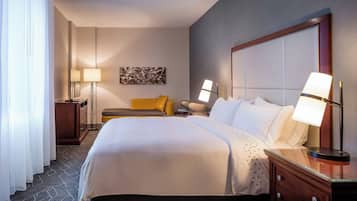 A hotel room with a large bed, two bedside tables with lamps, a nightstand, a sofa, and a wall-mounted artwork.