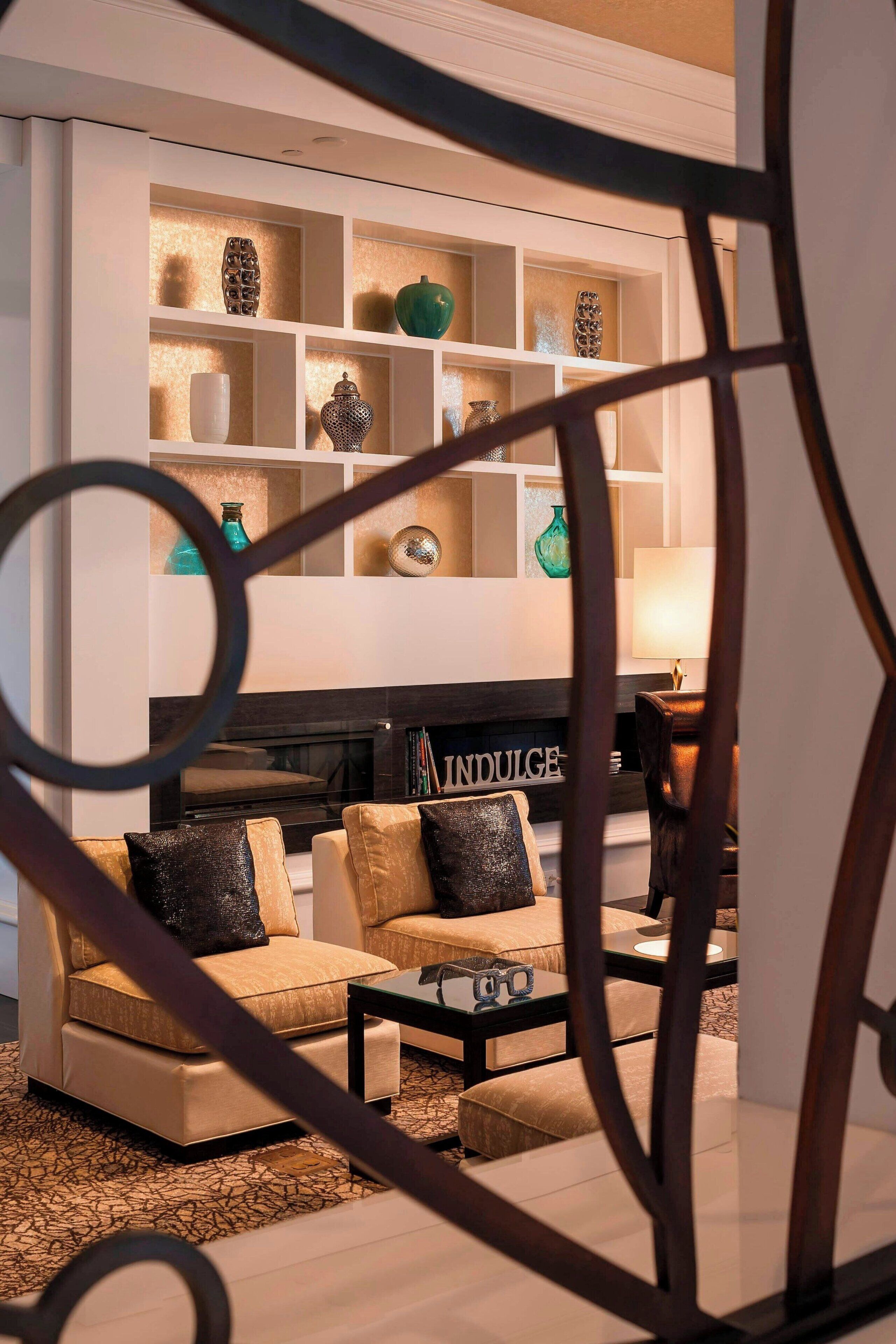 Una sala de estar moderna con chimenea, sofás y una mesa de centro. Se ven estanterías con objetos decorativos.