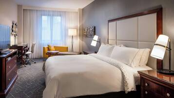 A hotel room with a large bed, a desk, a chair, and a TV.