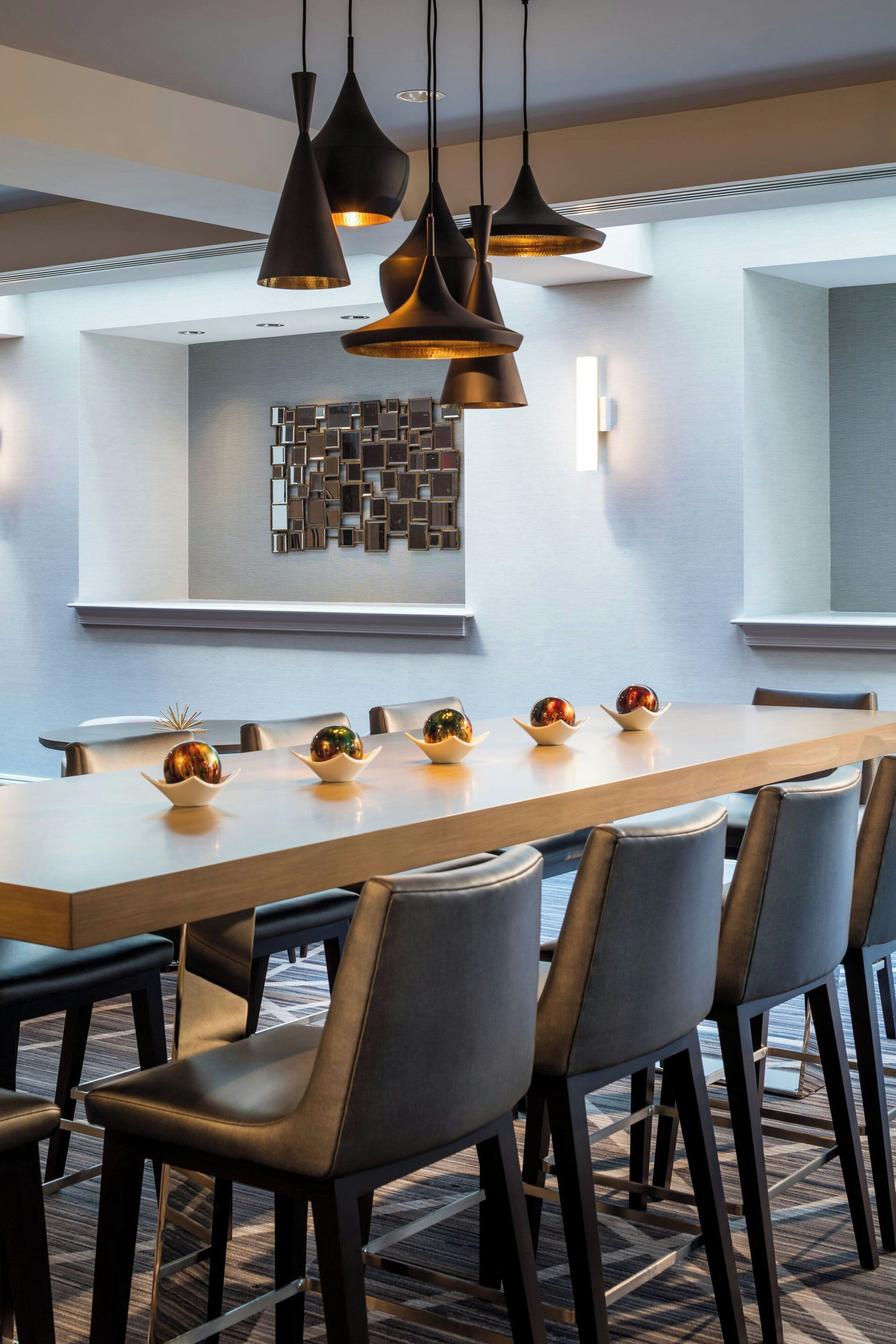 A modern dining area with a long table, multiple chairs, and pendant lighting.