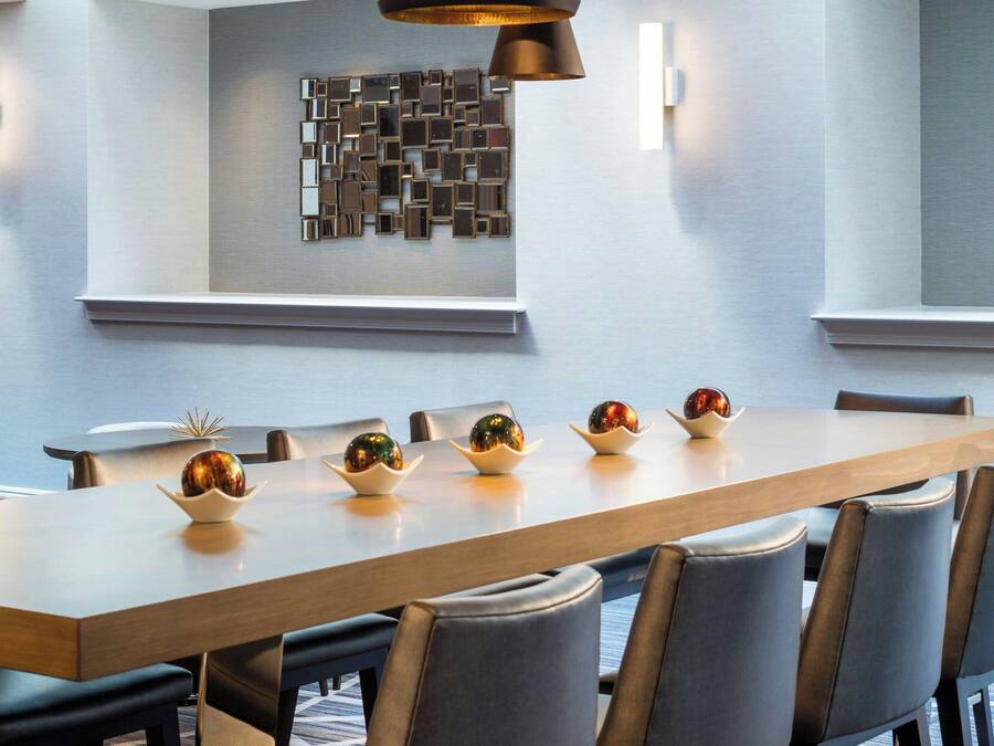 A modern dining area with a long table, multiple chairs, and pendant lighting.
