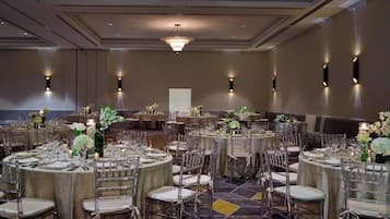 Un salón de banquetes con mesas redondas dispuestas para comer, cada una con sillas y cubertería.