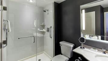 Un baño moderno con ducha de vidrio, inodoro blanco y tocador con un espejo grande.