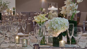 A banquet table set with multiple wine glasses, vases with white flowers, and candles.