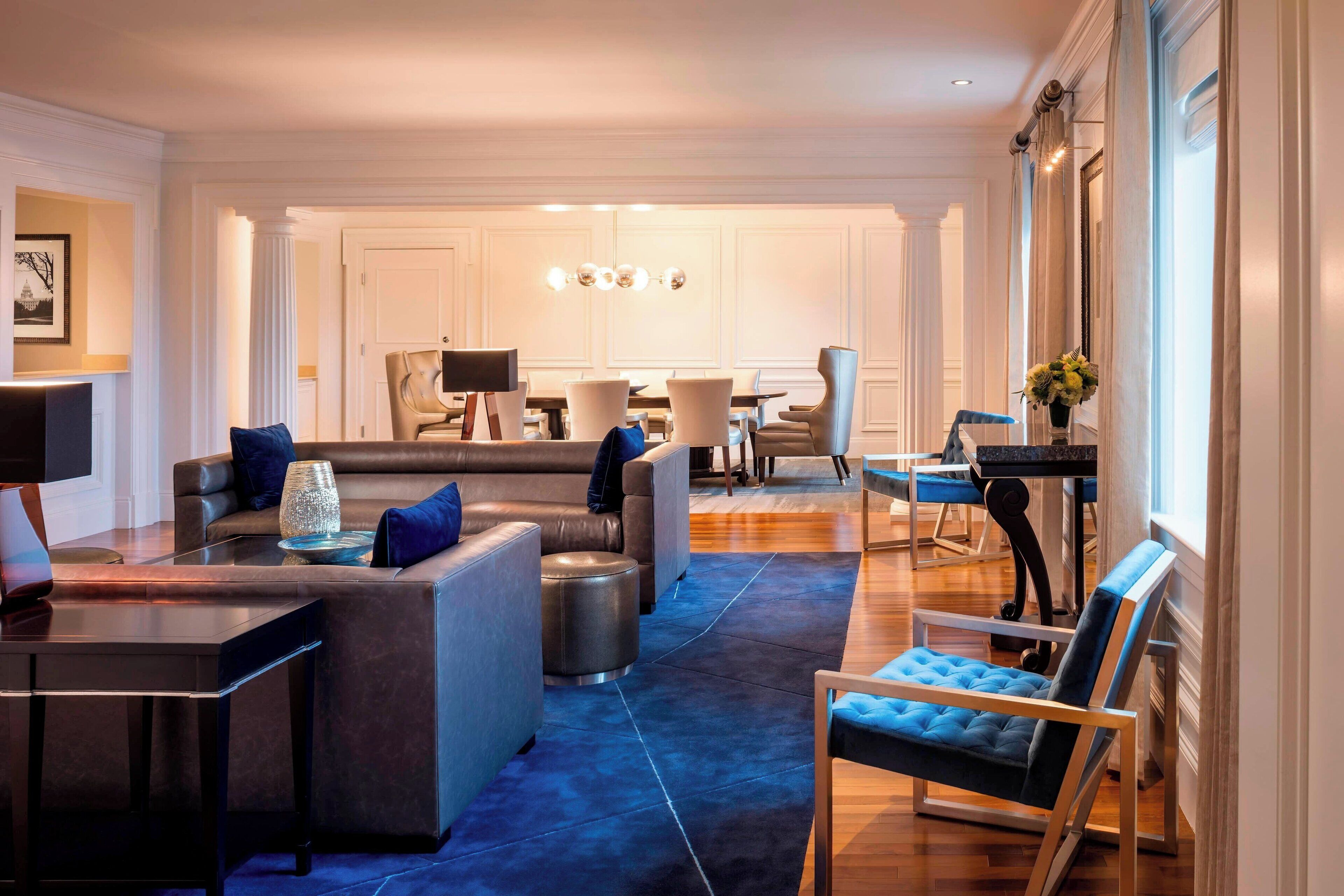 A modern living room with a sectional sofa, a coffee table, and a blue armchair. There is a dining area with a table and chairs in the background.