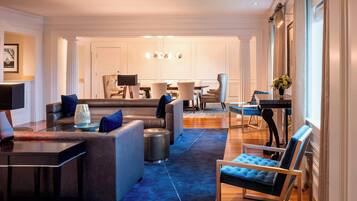 A modern living room with a sectional sofa, a coffee table, and a blue armchair. There is a dining area with a table and chairs in the background.