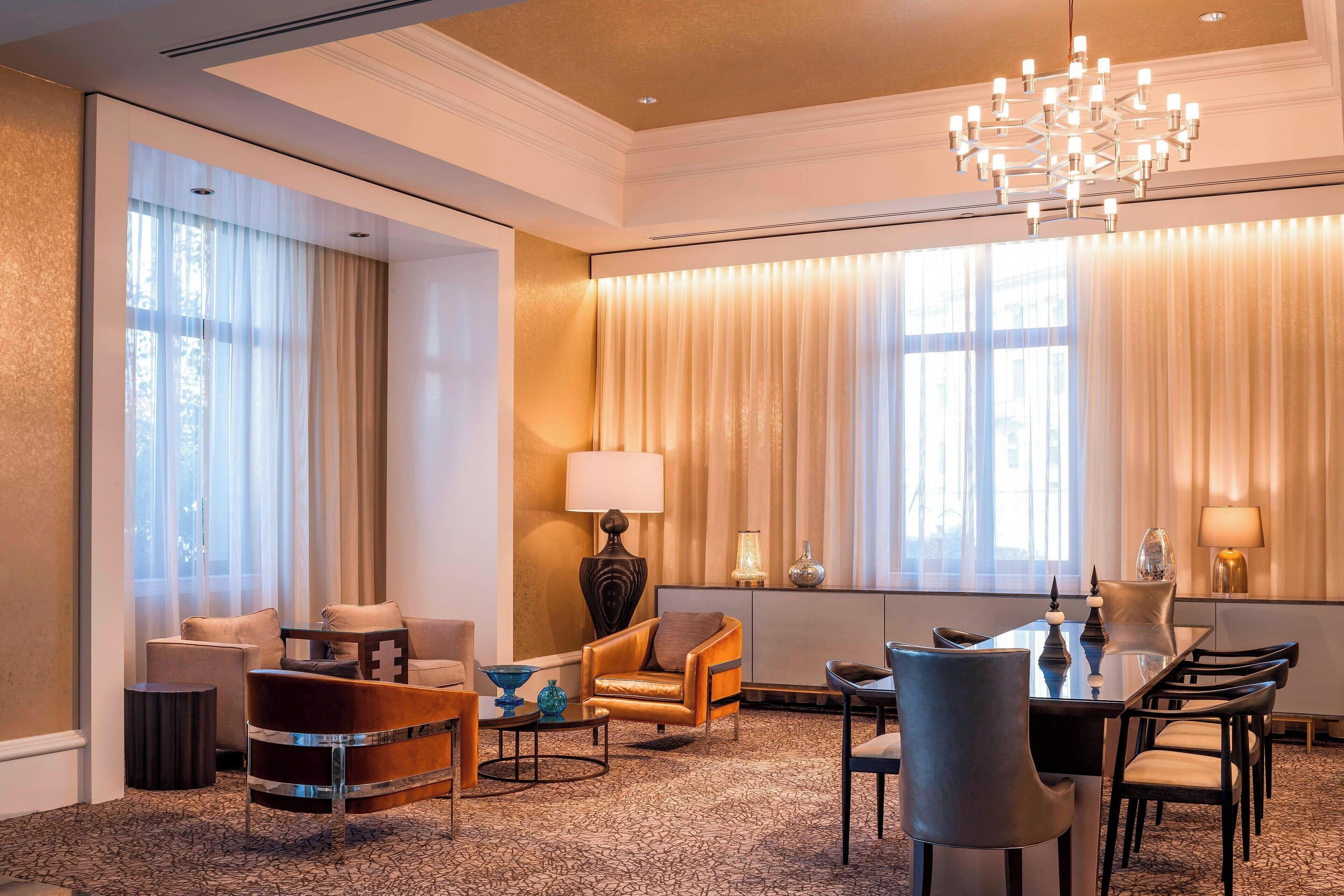 Ein Hotelzimmer mit großem Fenster, einer Kristallleuchtre, einem Esstisch mit Stühlen und einem Sofa.