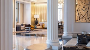 Um hall amplo com piso de mármore, colunas brancas, um lustre moderno e uma área de estar com sofás de couro.