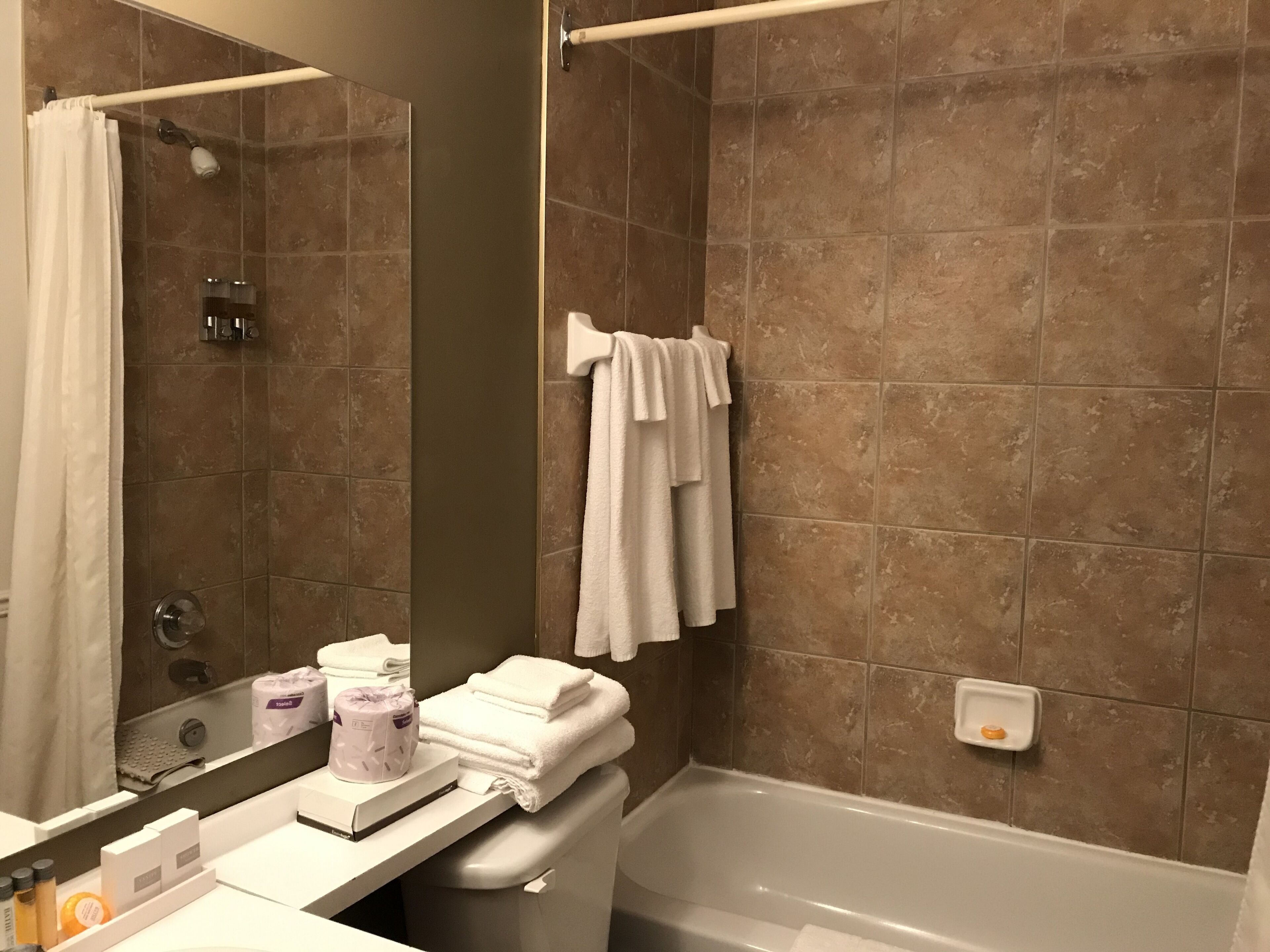 A bathroom with a bathtub, a shower, and a sink. There are towels and toiletries on the counter.
