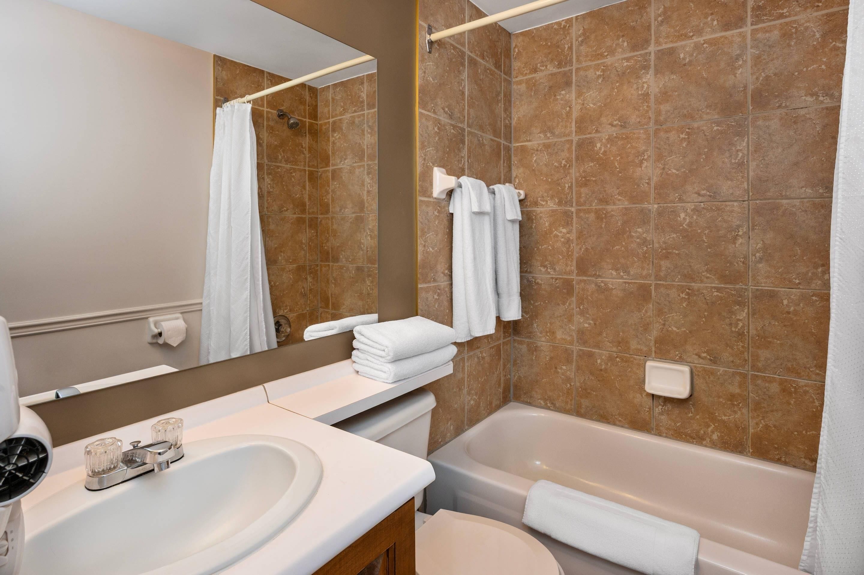 Une salle de bain équipée d’un lavabo, d’un miroir, d’une baignoire et de serviettes.