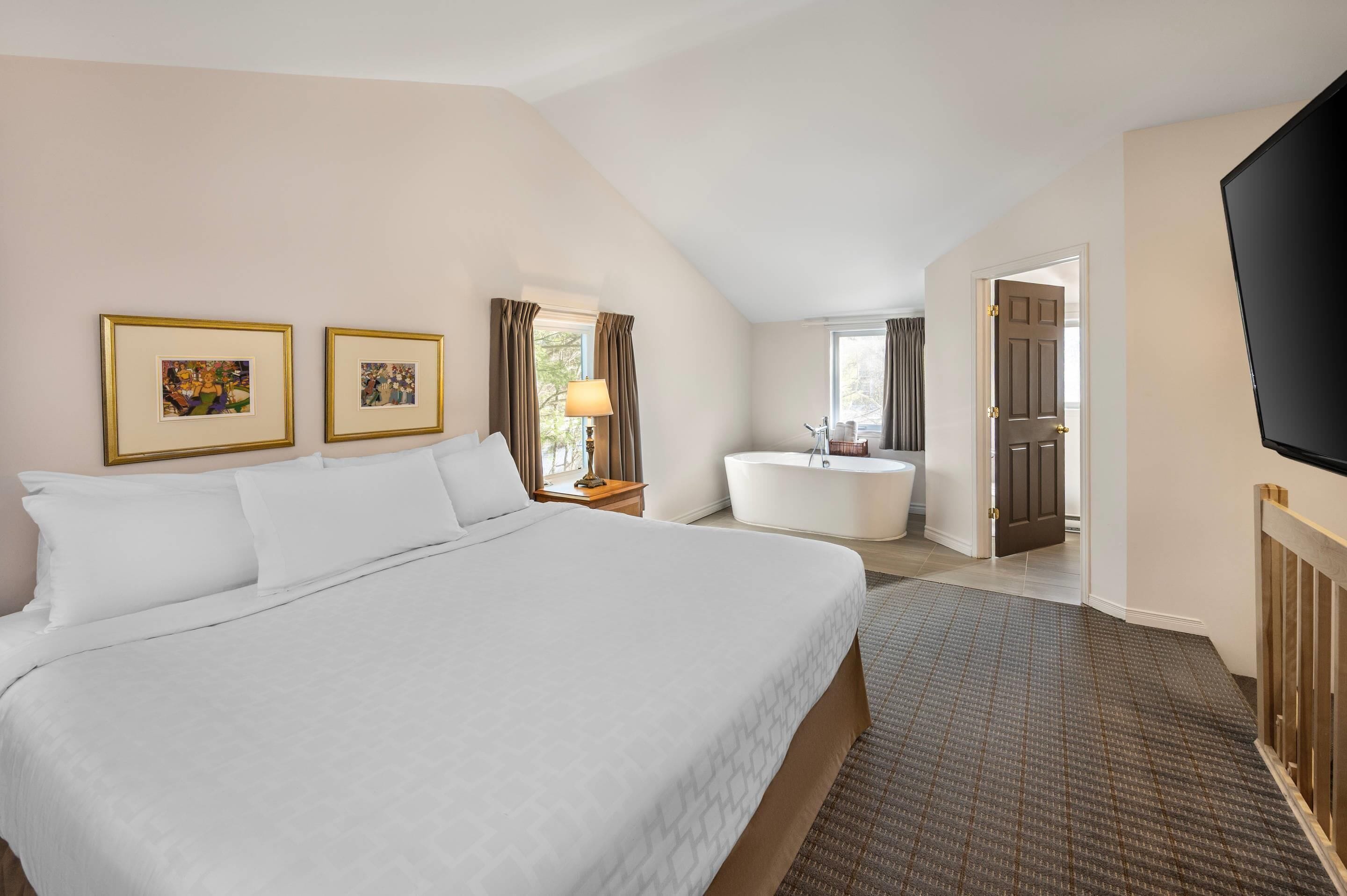 A hotel room with a large bed, a bathtub, and a TV.
