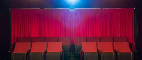 A theater with red curtains, rows of black seats, and two ceiling lights.