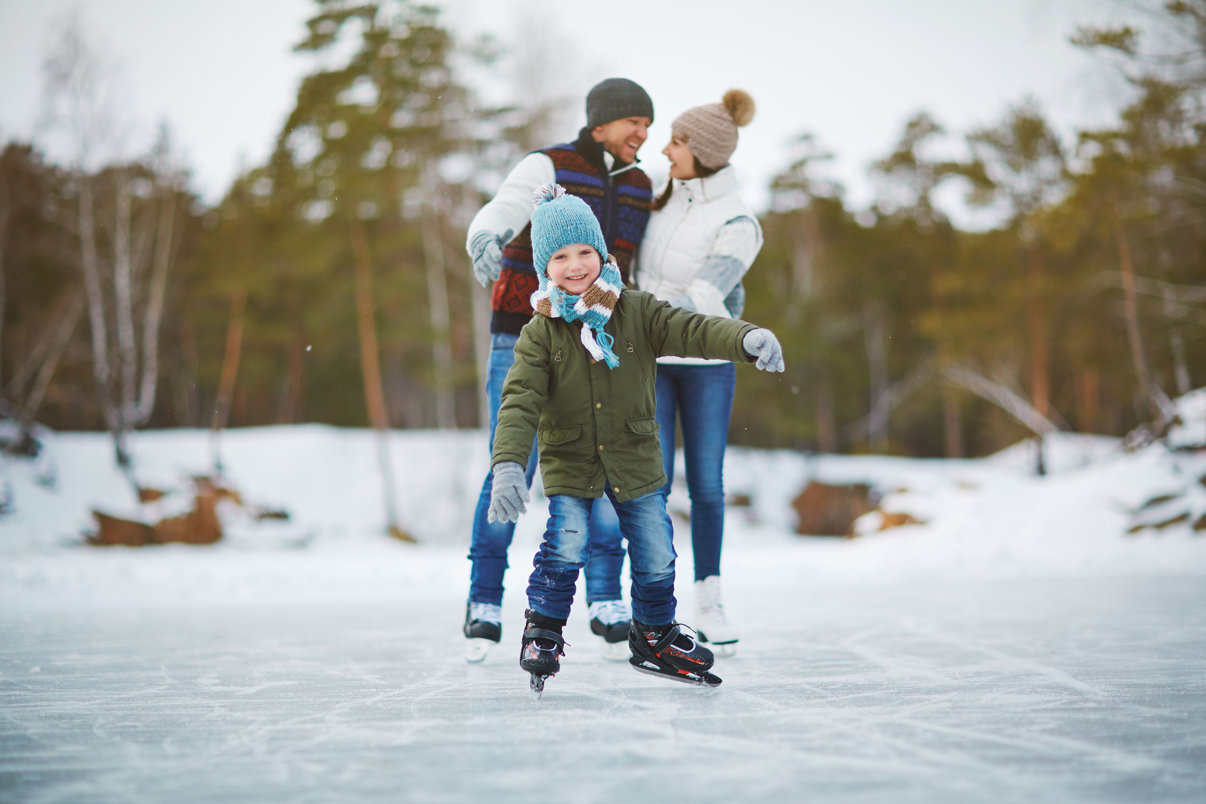 A family on ice skates on a frozen lake with trees in the background.