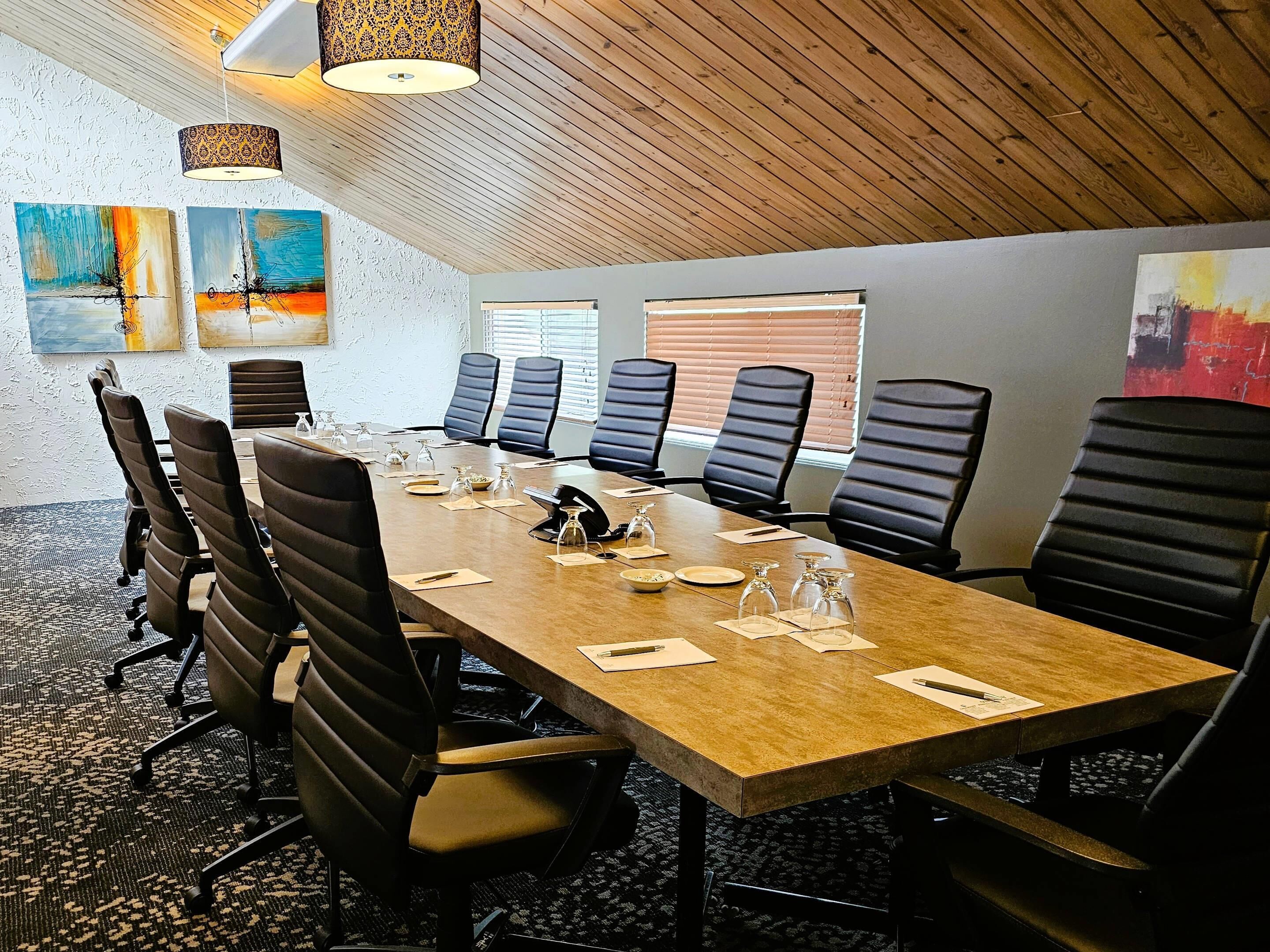 Un salón de conferencias con una larga mesa, sillas negras y techo de madera.