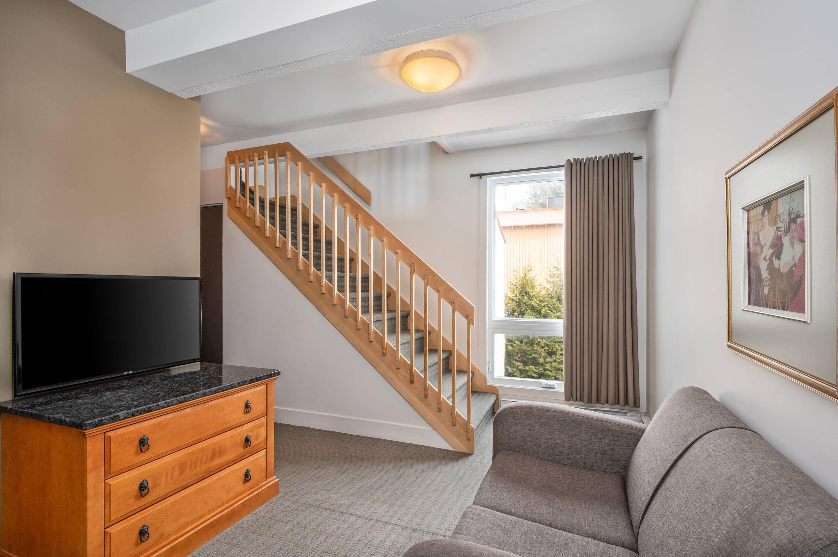 A living room with a TV, wooden staircase, and a sofa.