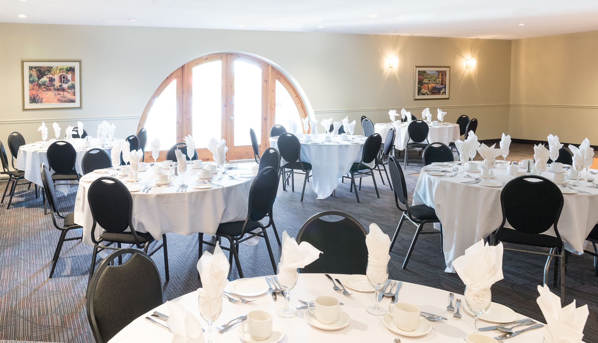 A banquet hall with round tables set for dining, black chairs, and white tablecloths.