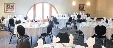 A banquet hall with round tables set for dining, black chairs, and white tablecloths.