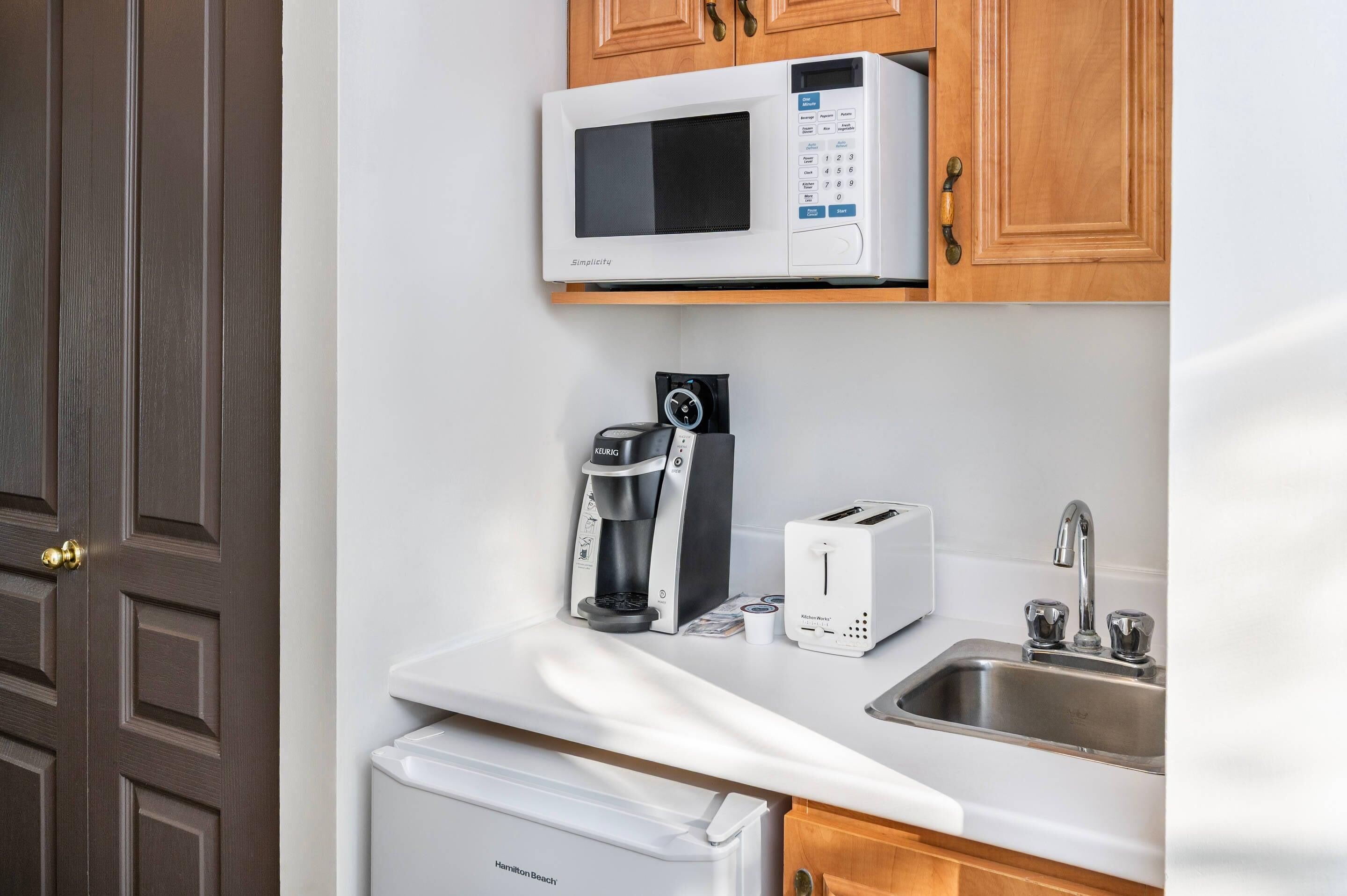 A kitchen with a microwave, coffee maker, toaster, and sink.