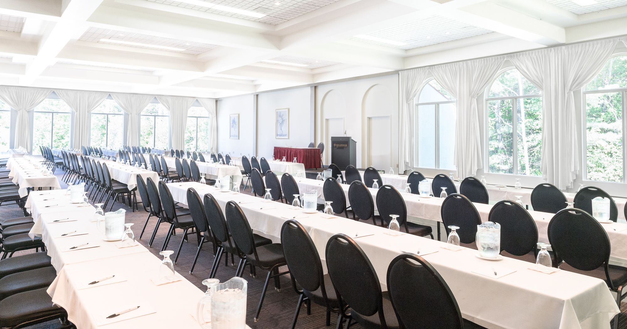 A large conference room with long tables and chairs, large windows, and a podium.