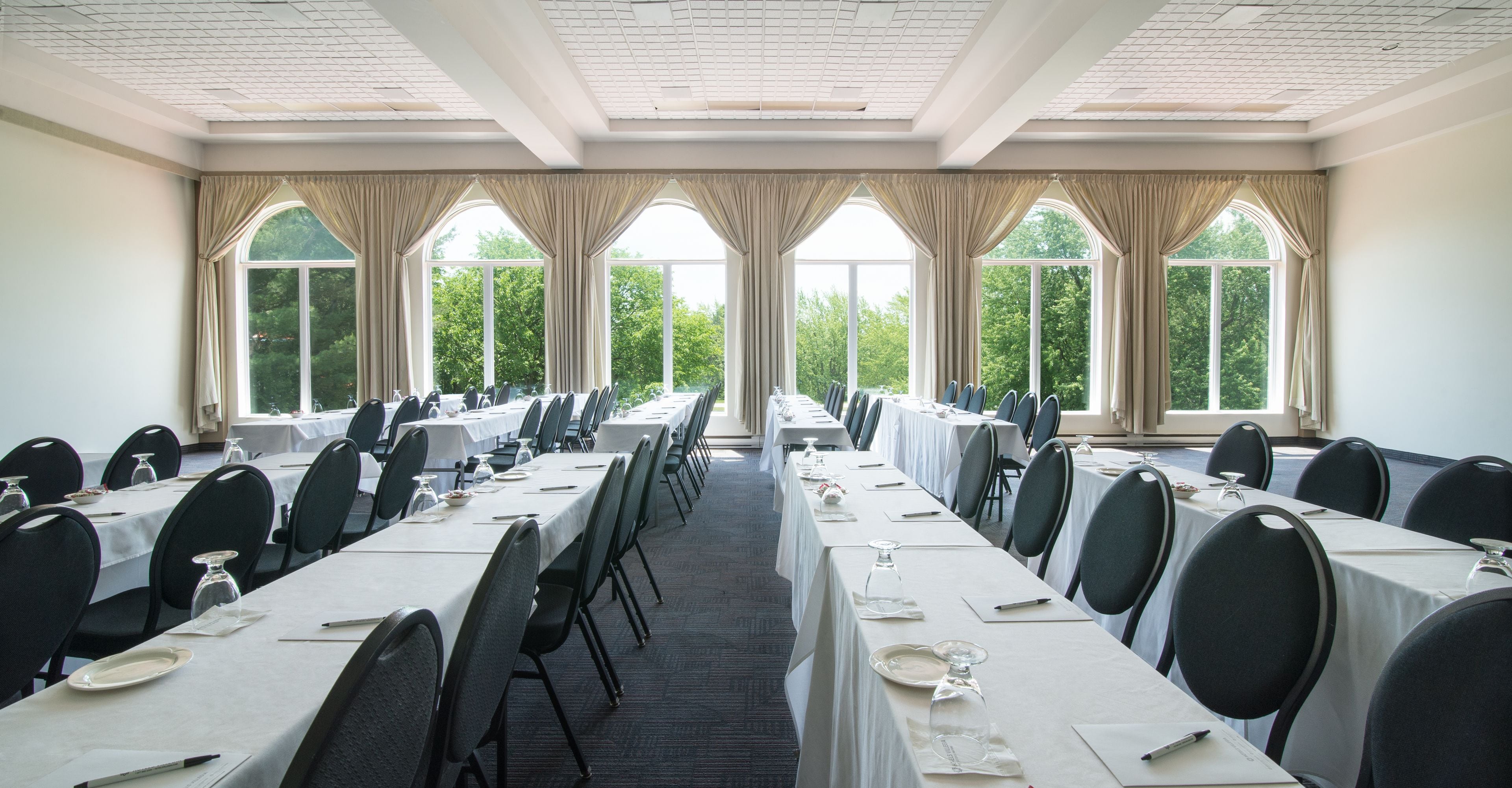 A conference room with long tables, chairs, and large windows with curtains.