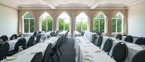 A conference room with long tables, chairs, and large windows with curtains.