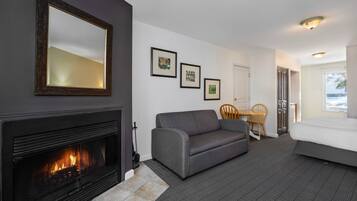 Una habitación de hotel con chimenea, un sofá, una cama, una mesa de comedor con sillas y cuadros en la pared.