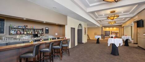 A bar area with a long counter, multiple stools, and a variety of bottles and glasses.