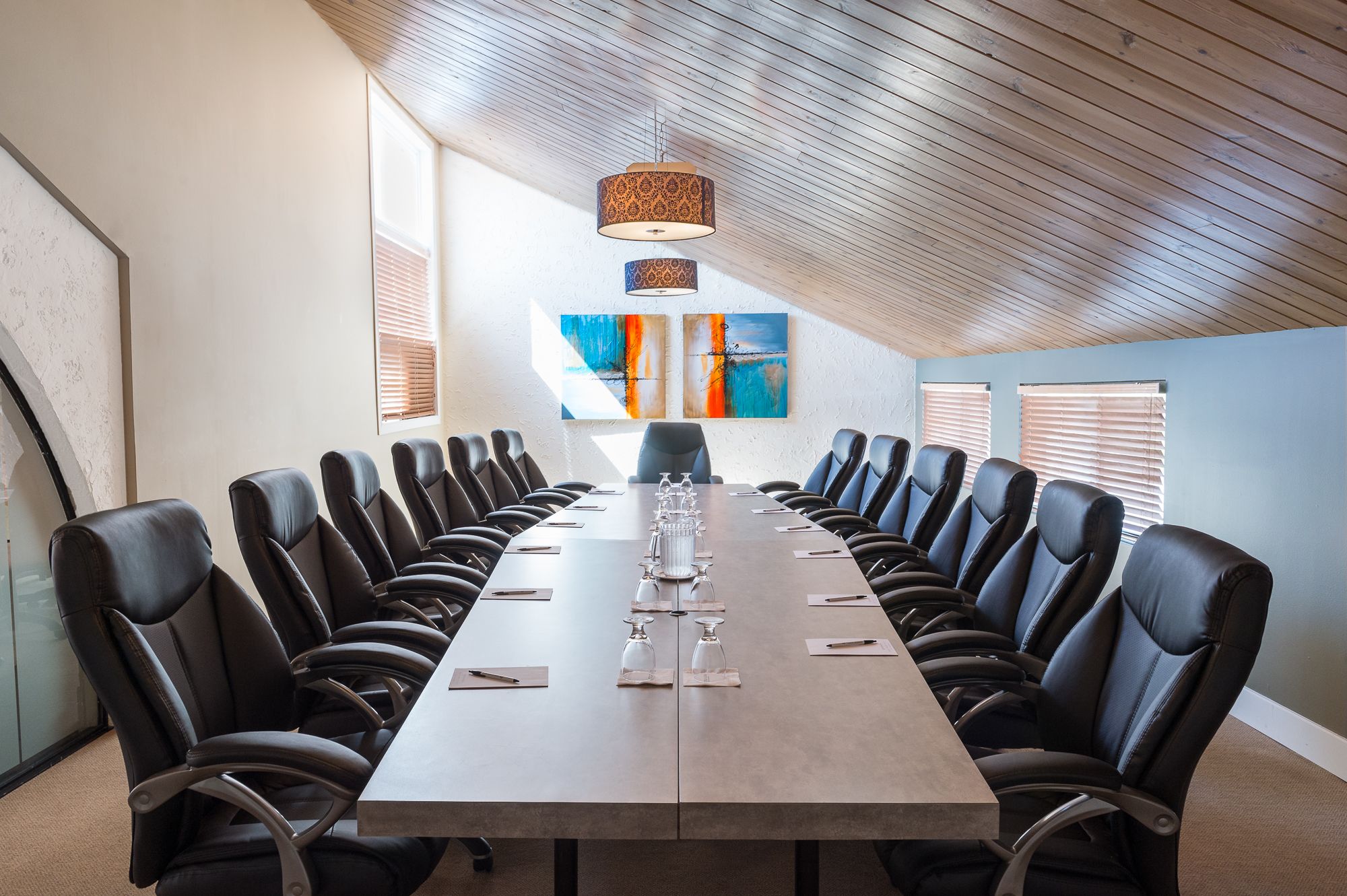 A conference room with a long table, black leather chairs, and a wooden ceiling.