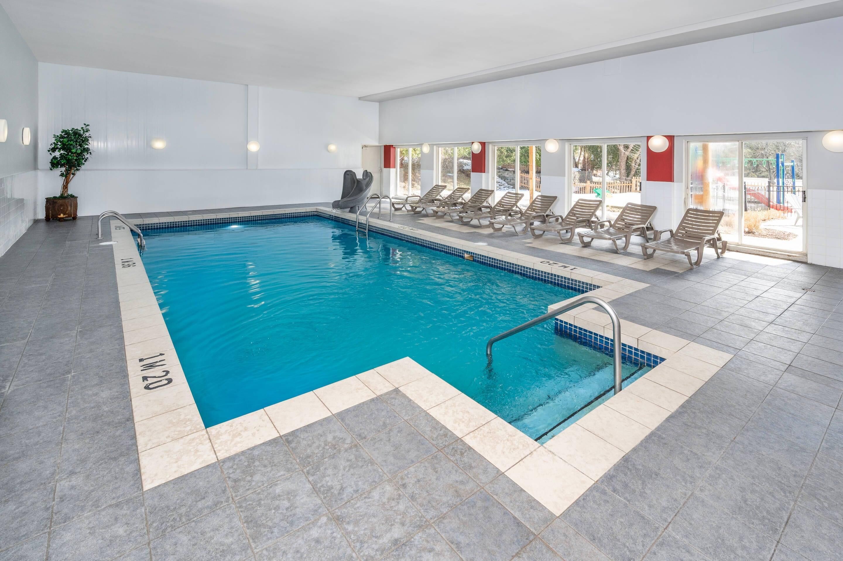 Une piscine intérieure à l’eau claire, avec un toboggan et des chaises longues disposées le long du bord.