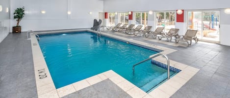 Une piscine intérieure à l’eau claire, avec un toboggan et des chaises longues disposées le long du bord.