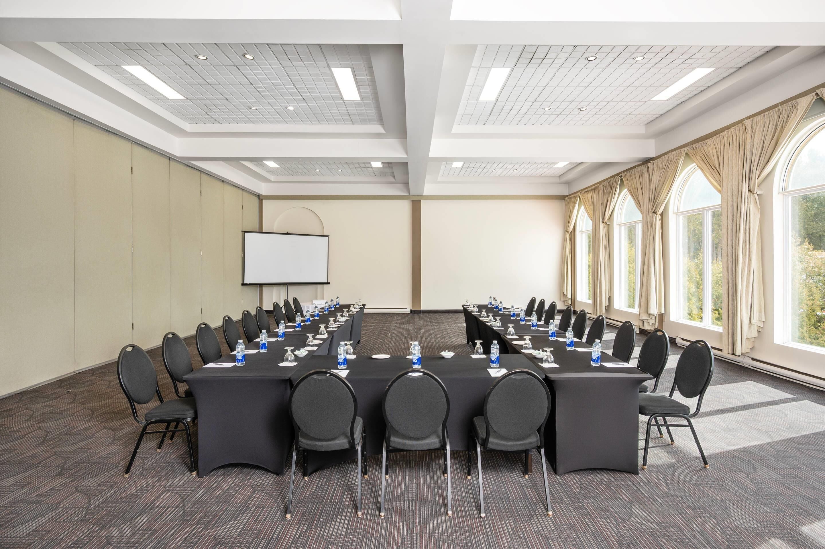 A conference room with a long table, chairs, water bottles, and a projector screen.