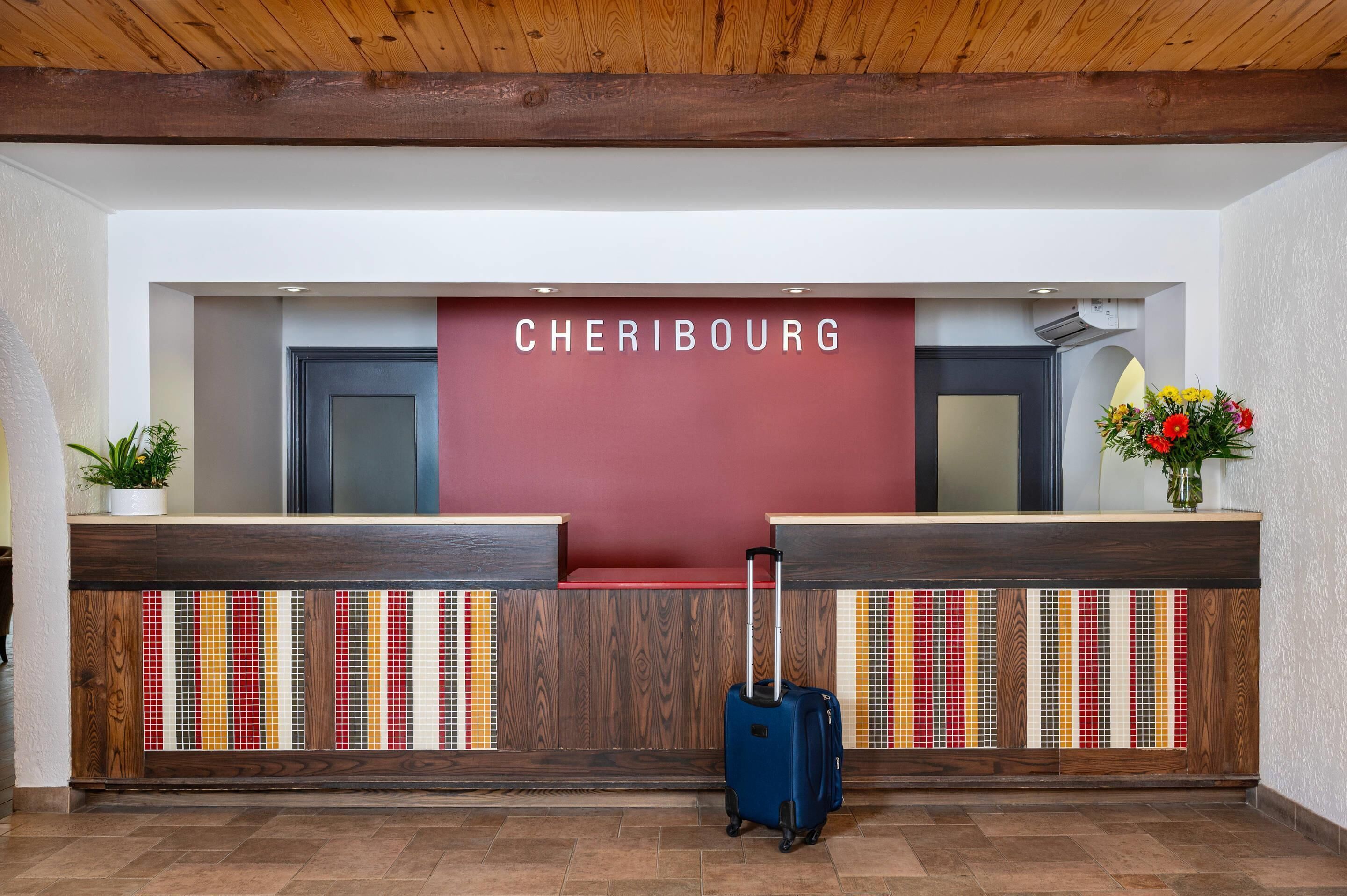 Un comptoir d'accueil avec une pancarte indiquant « CHERIBOUG » et une valise bleue devant.