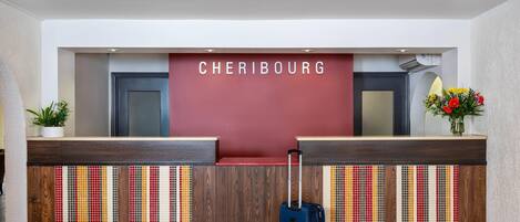 Taulell de recepció amb un cartell que diu 'CHERIBOUG' i una maleta blava al davant.