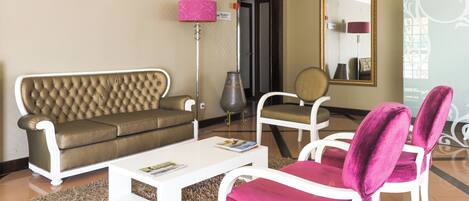 A living room with a brown leather sofa, a white coffee table, and two white chairs with pink cushions.