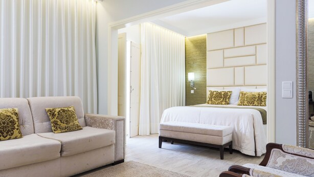 A hotel room with a large bed, a sofa, and a chair. There is a mirror on the wall and a light fixture above the bed. - Josefa D'Óbidos (Obidos)
