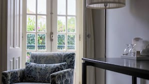 A room with a patterned armchair, a table with a lamp, and a view through a large window. - Josefa D'Óbidos (Obidos)