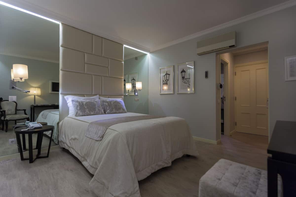 Habitación de hotel con una cama grande, una mesita de noche, una silla, un espejo y una puerta.